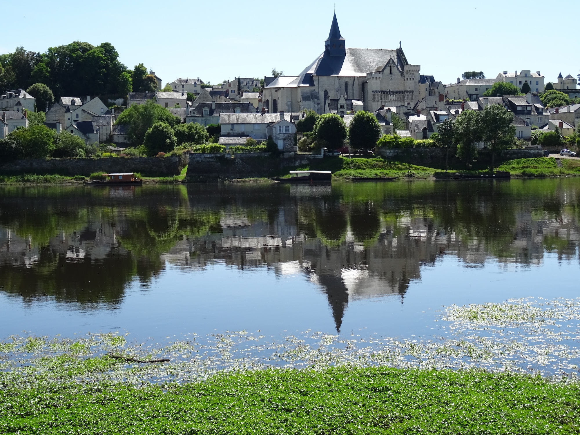 The old stone abbey and the village of Candes St Martin reflecting in the river in France on a hot summer day
