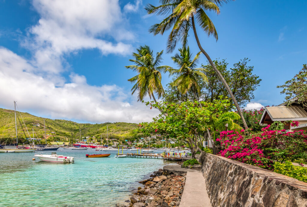 Bright and colorful image of Bequia. Palm trees at the water, blue sky and white clouds, boats in the harbor of Port Elisabeth. Saint Vincent and the Grenadines.