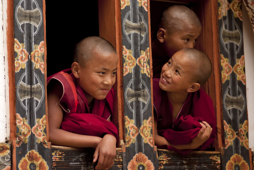 "Bumthang, Bhutan aA June 27, 2012: Three young Buddhist monks peer out from a monastery window at a local festival in the Bumthang Valley of Bhutan."