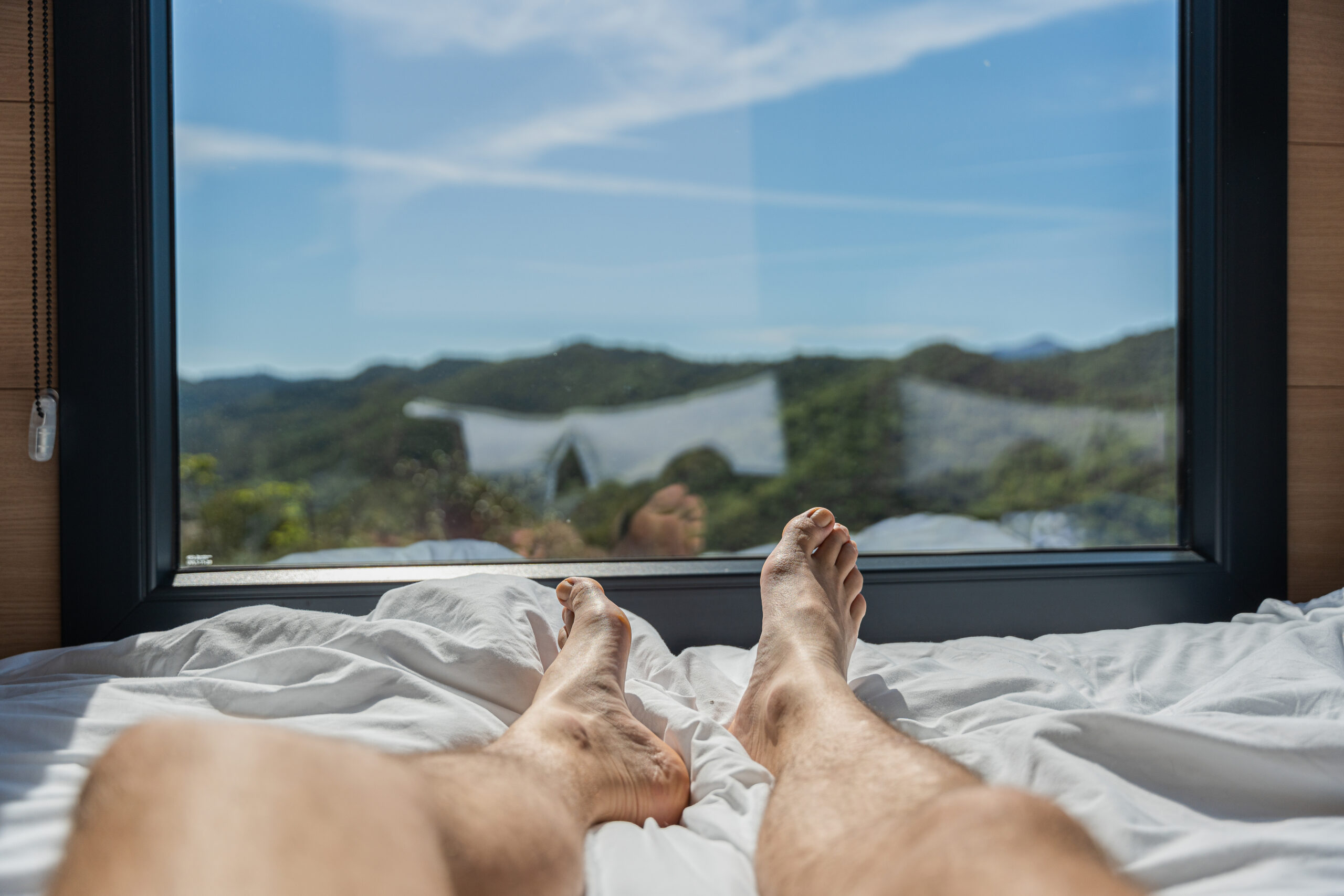 First point of view of man's feet relaxing in bed with mountain views. Feeling of freedom and peace.
