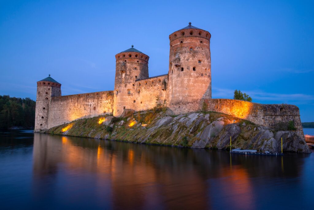 Illuminated stone towers of Olavinlinna Castle reflected in the water at Savonlinna