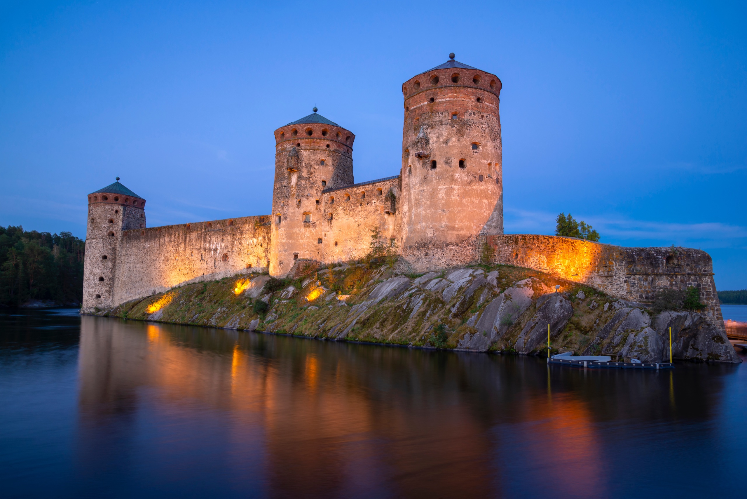 Illuminated stone towers of Olavinlinna Castle reflected in the water at Savonlinna